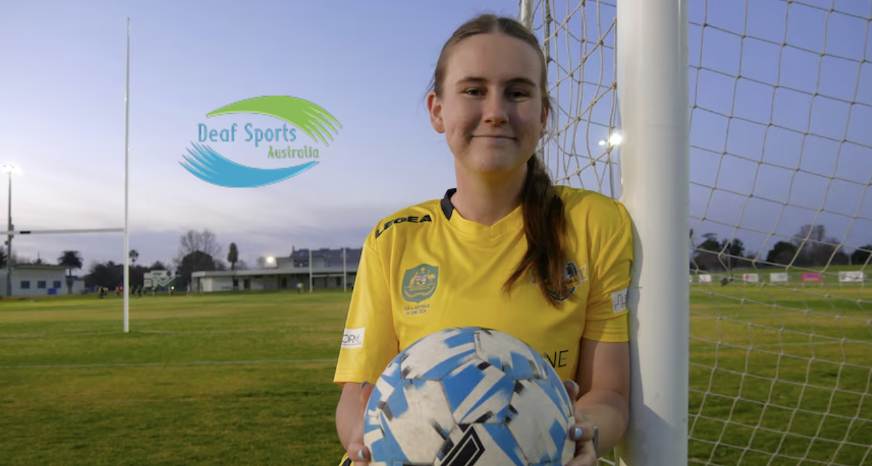 A soccer player (Ruby Miller) wearing a yellow jersey stands in front of the goal net on an outdoor field at sunset, holding a blue and white soccer ball. The Deaf Sports Australia logo appears in the sky area to the left.