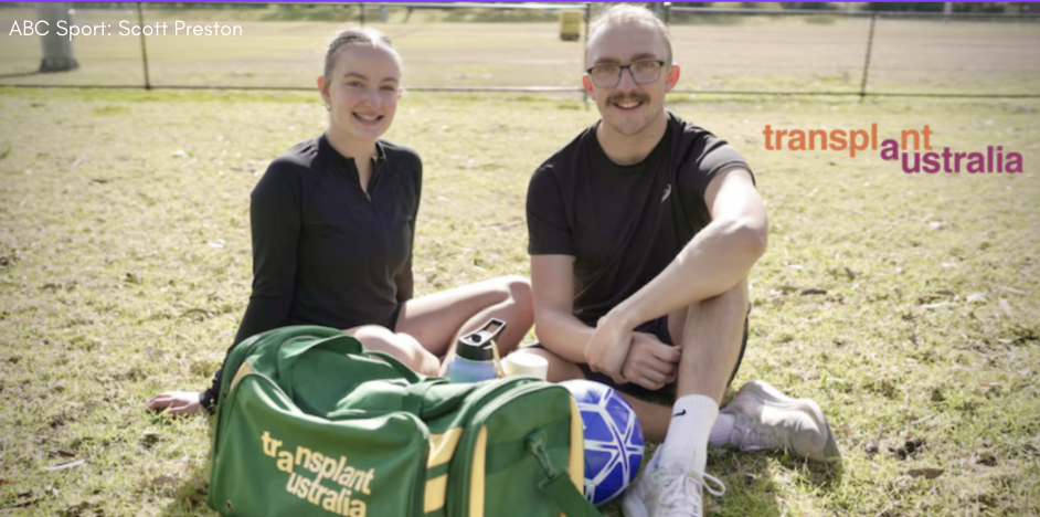 Two siblings in black athletic clothes are sitting on the grass in a sunlit outdoor field, with a blue soccer ball and a green and yellow sports bag labeled "transplant australia" in front of them. The Transplant Australia logo appears in orange and purple text on the right side of the image.