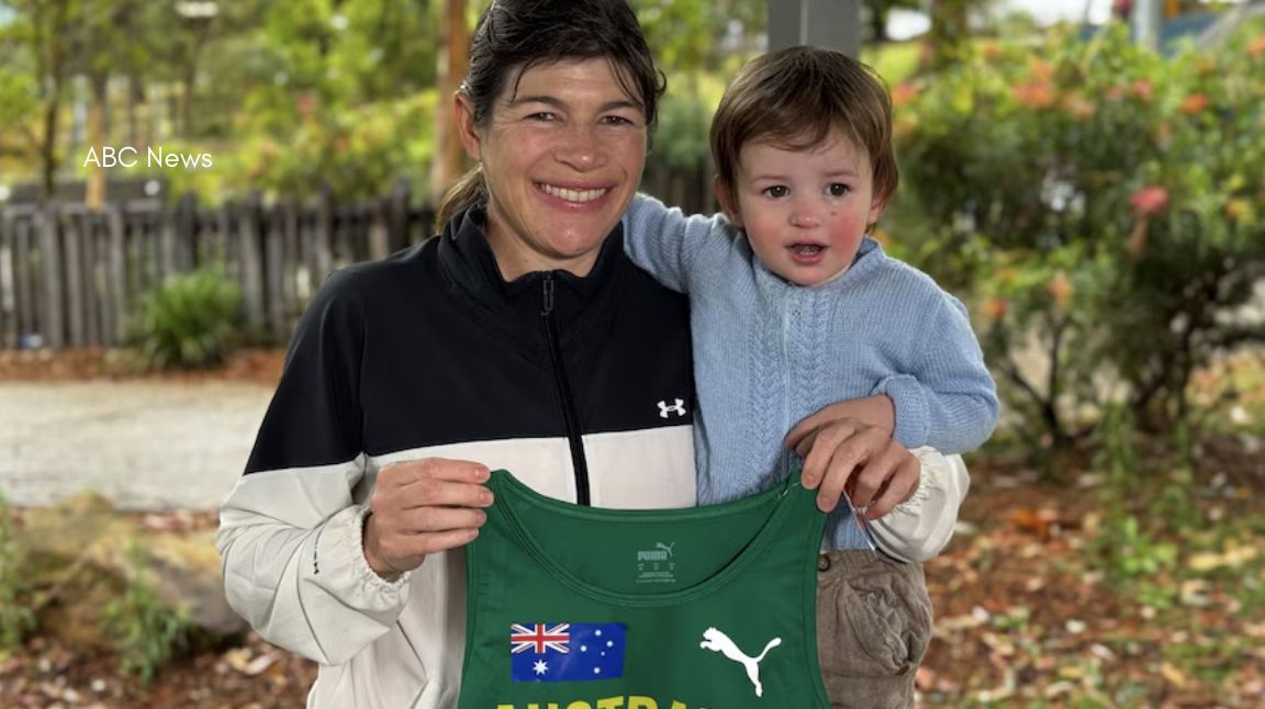 Australian marathon runner Melinda Vernon smiles and stands with her young son Hugo outdoors, proudly holding her green “Australia” athletics singlet as they prepare for the Deaflympics, with “ABC News” text visible in the corner.